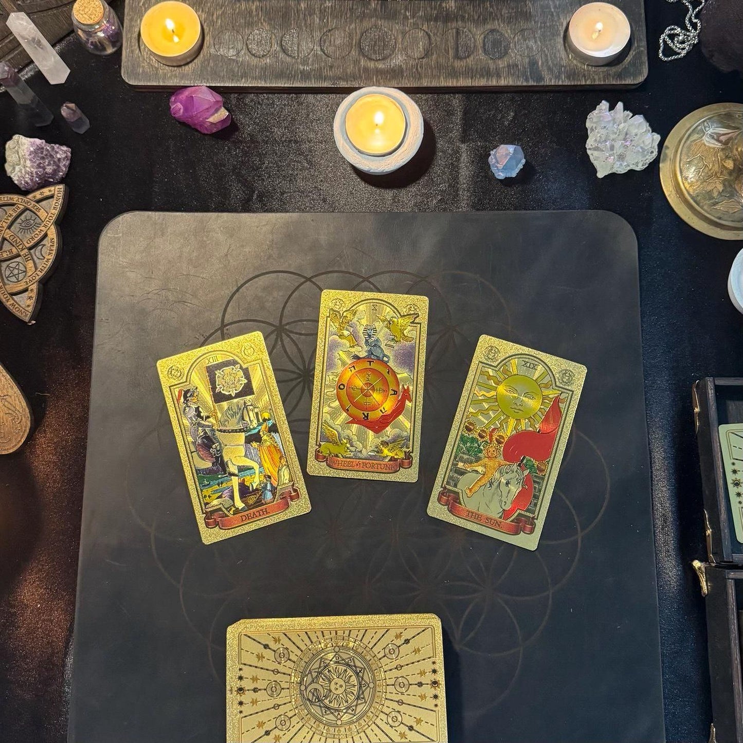 a tarot card spread on a black surface, with three cards arranged in a triangular formation. The cards feature intricate designs and illustrations, suggesting a spiritual or mystical theme.
