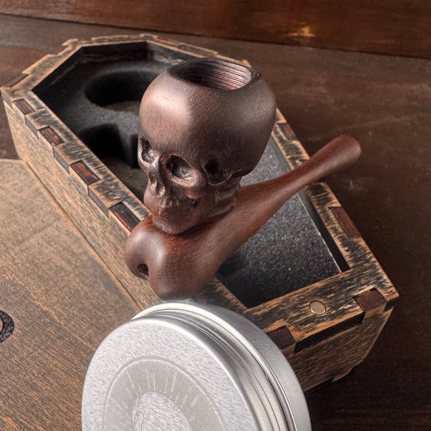 a wooden pipe with a skull-shaped handle, placed inside a wooden box with a metal lid.