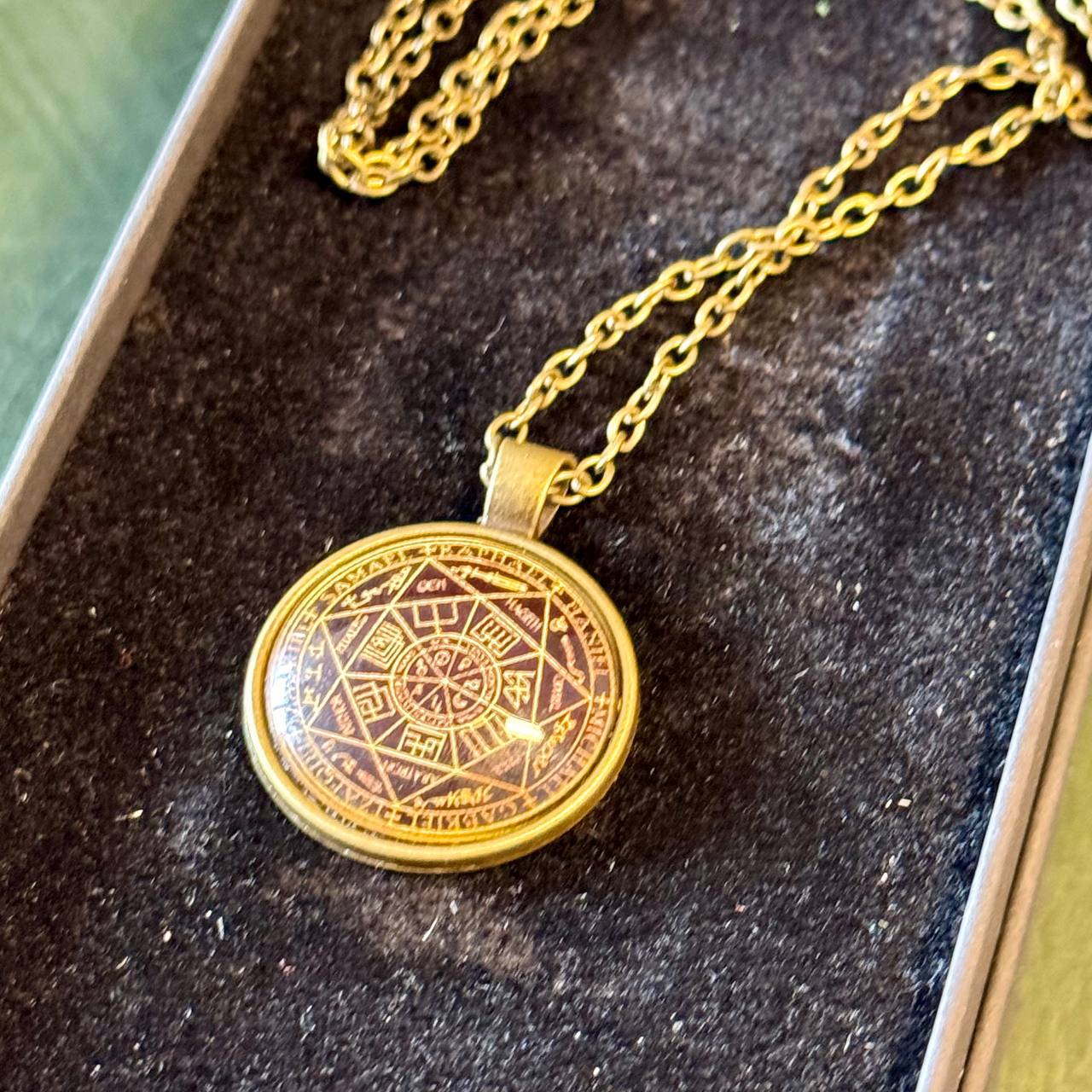 A gold-colored pendant necklace with a circular medallion featuring an intricate design.