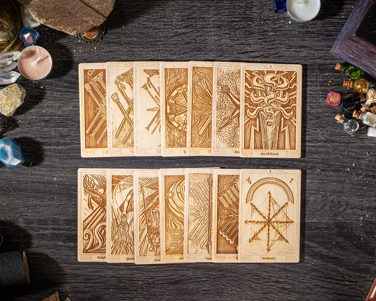 A collection of wooden tarot cards arranged on a dark wooden surface, with various intricate designs and illustrations.