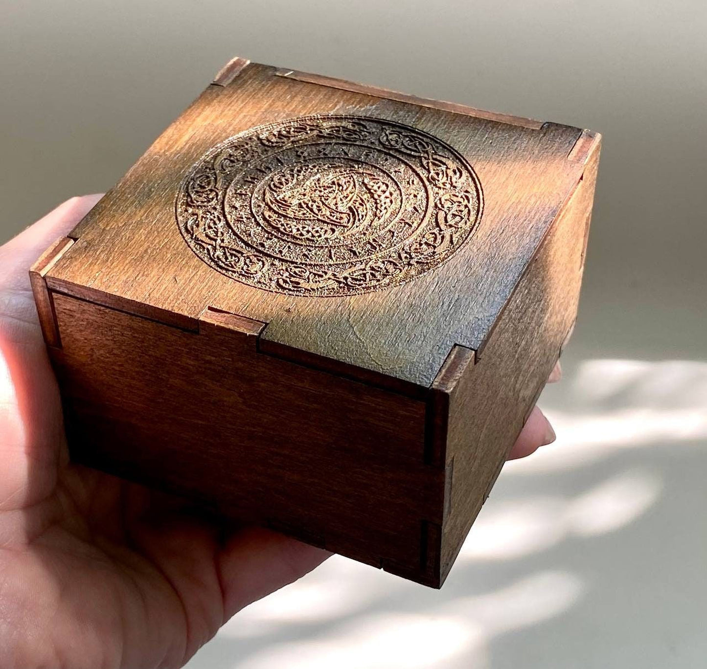 A hand is holding a wooden box with an intricate carved design on the front.