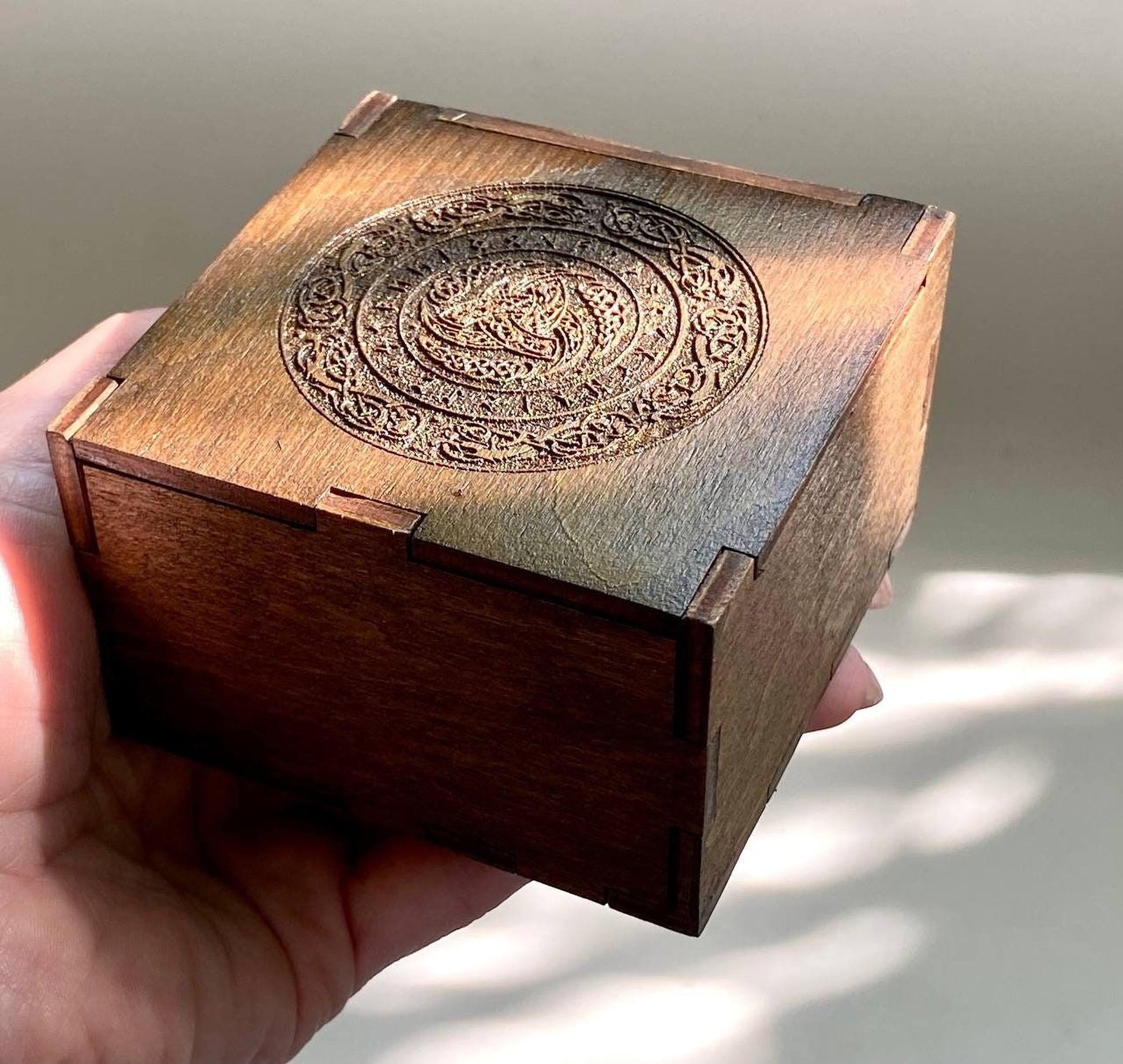 A hand is holding a wooden box with an intricate carved design on the front.