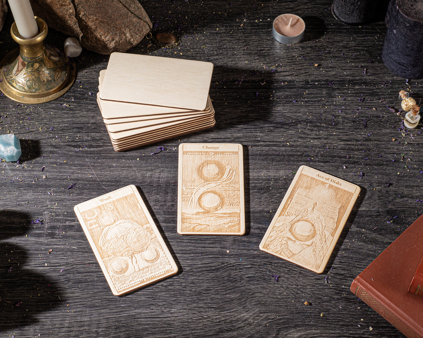 three wooden tarot cards with intricate designs, placed on a dark wooden surface alongside various objects such as candles, crystals, and books.