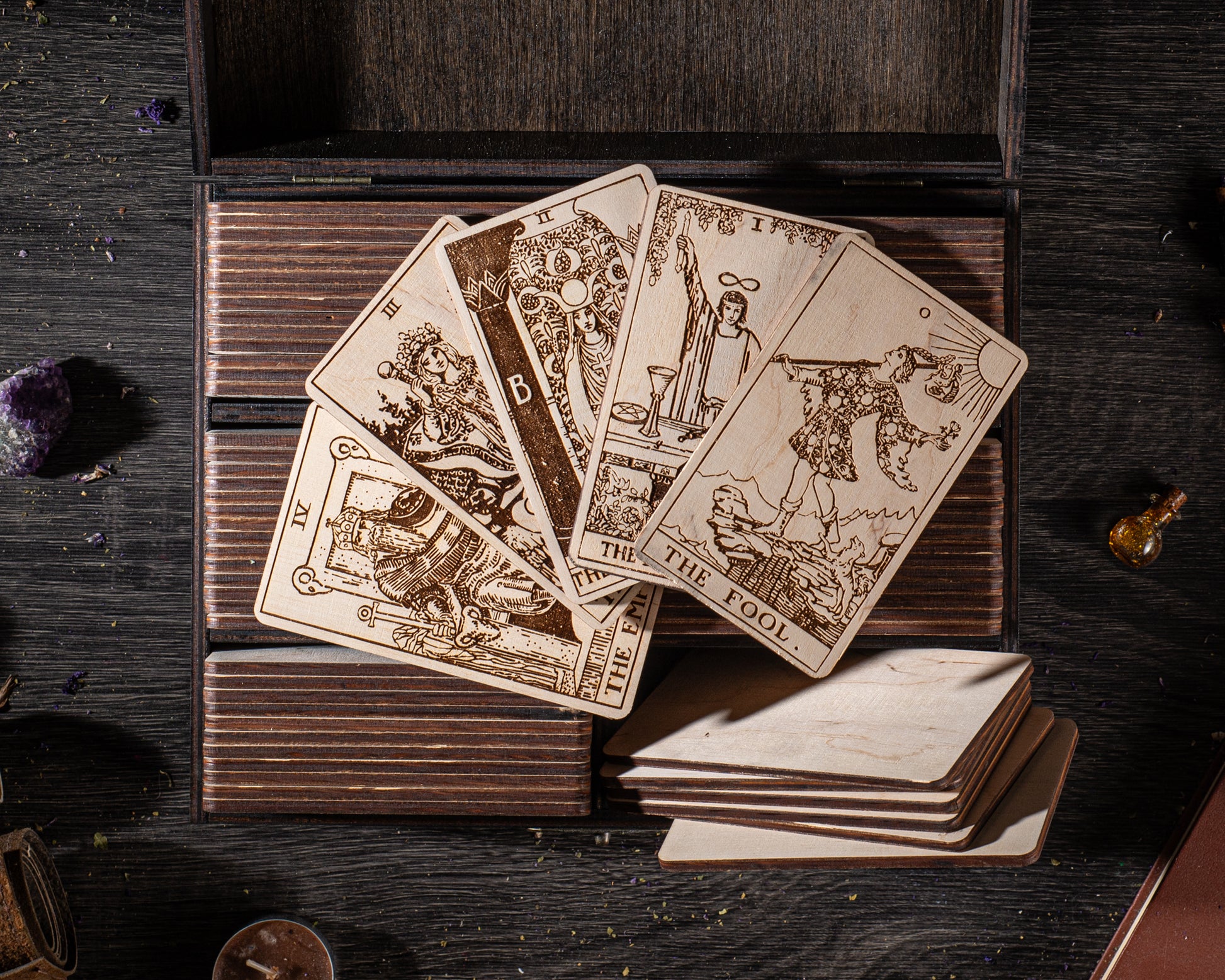 A wooden deck with a deck of tarot cards and a small bottle of oil on it, along with some crystals and a book.