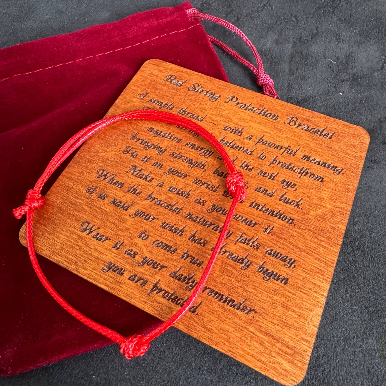 A wooden plaque with a red string bracelet tied around it, placed on a dark surface.