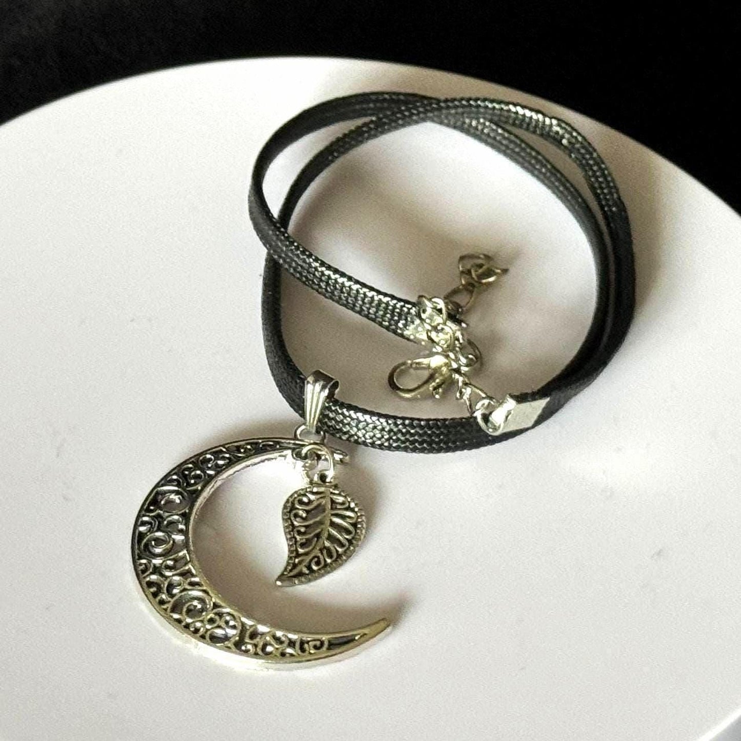 A silver necklace with a pendant featuring a crescent moon and a leaf-shaped charm.