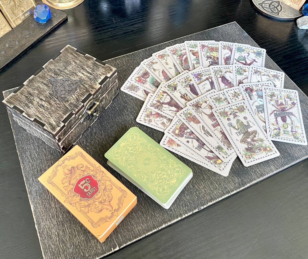 a collection of tarot cards and a box of playing cards arranged on a wooden surface.