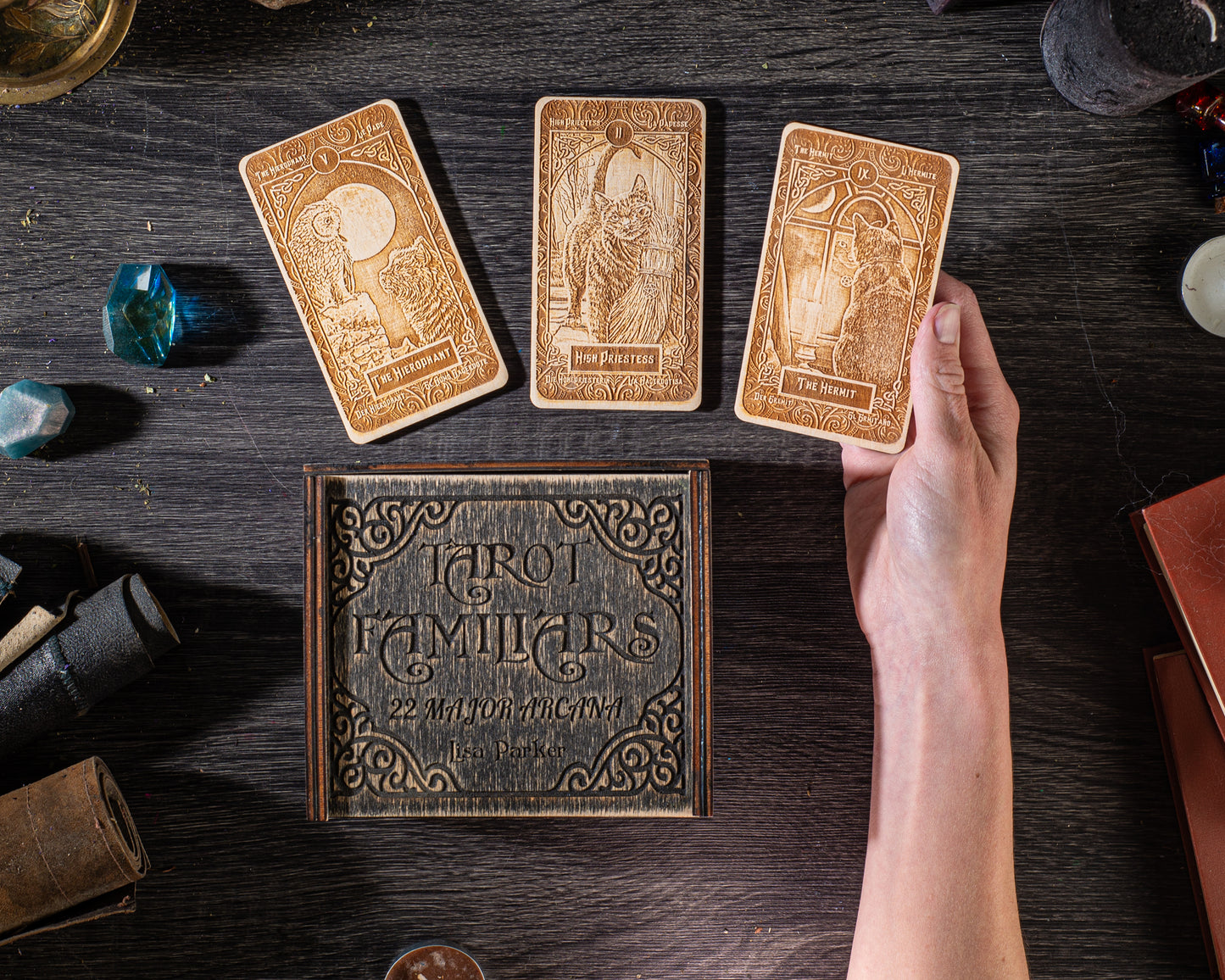 a wooden box with the title "Tarot Familiars" and a hand holding a tarot card, along with various objects such as a book, a crystal, and a candle on a wooden surface.