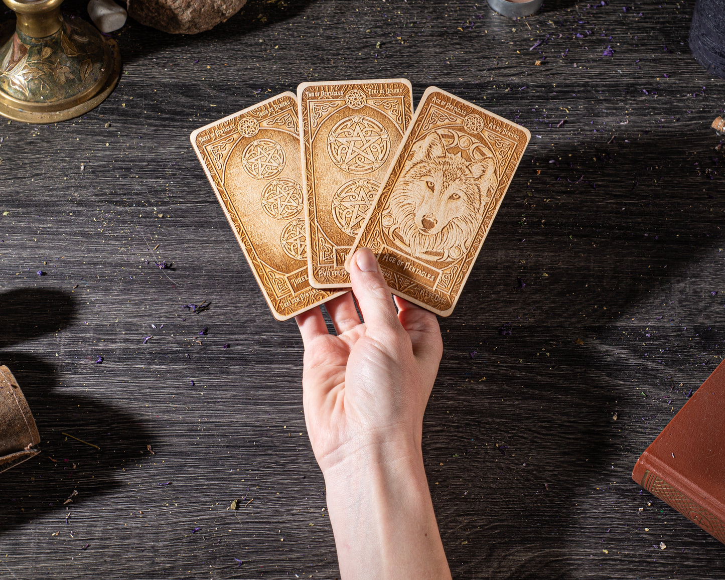 A hand holding three wooden tarot cards with intricate designs on them, placed on a dark wooden surface.