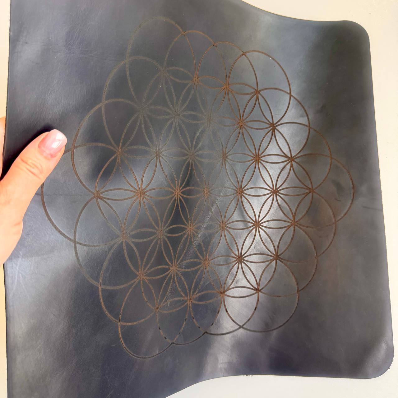 A hand is holding a black leather object with a repeating pattern of circles on it.