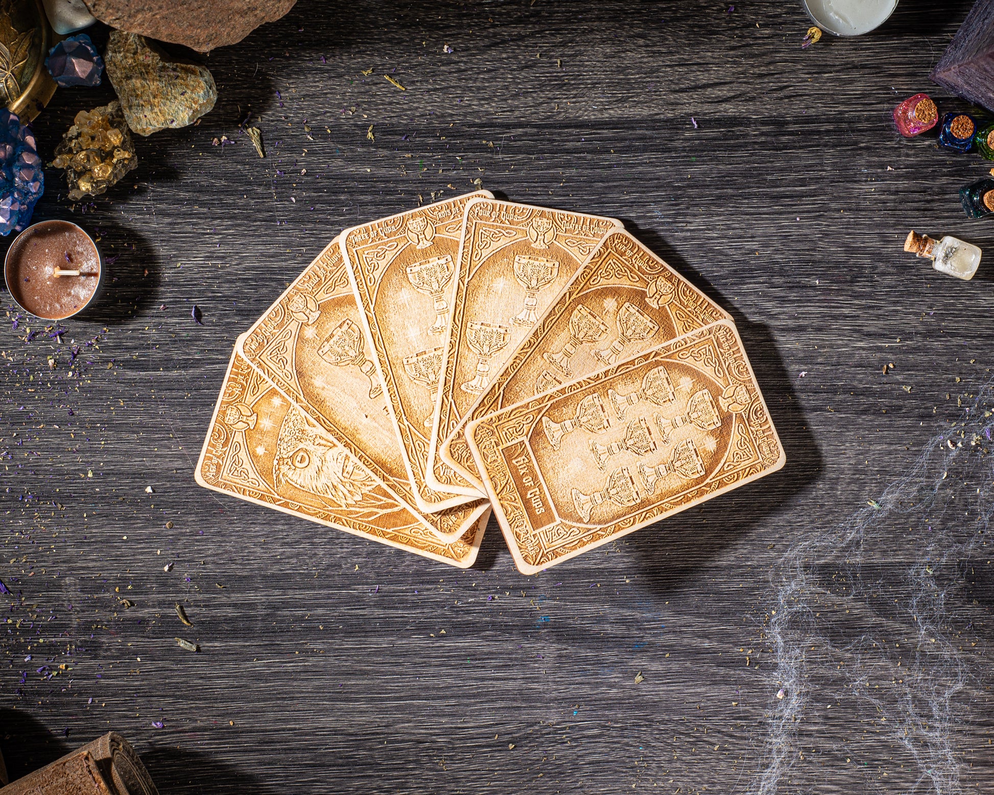 a deck of playing cards arranged on a wooden surface, with various objects such as crystals, a candle, and a small bottle nearby.