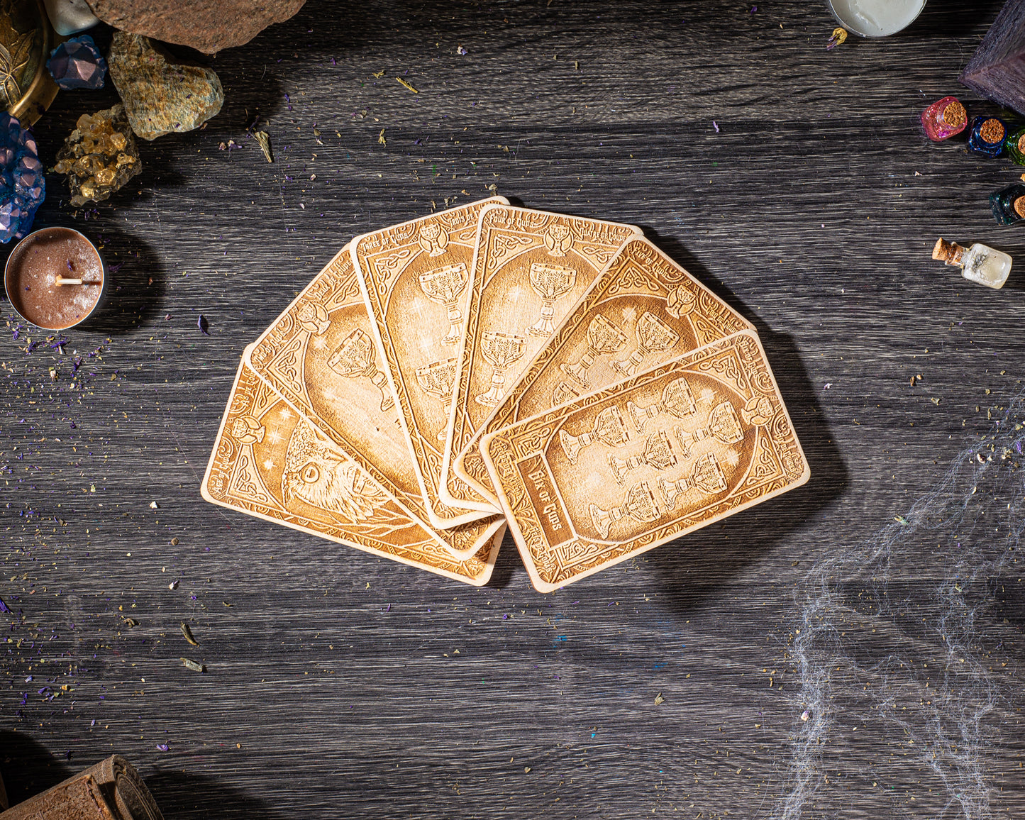a deck of playing cards arranged on a wooden surface, with various objects such as crystals, a candle, and a small bottle nearby.