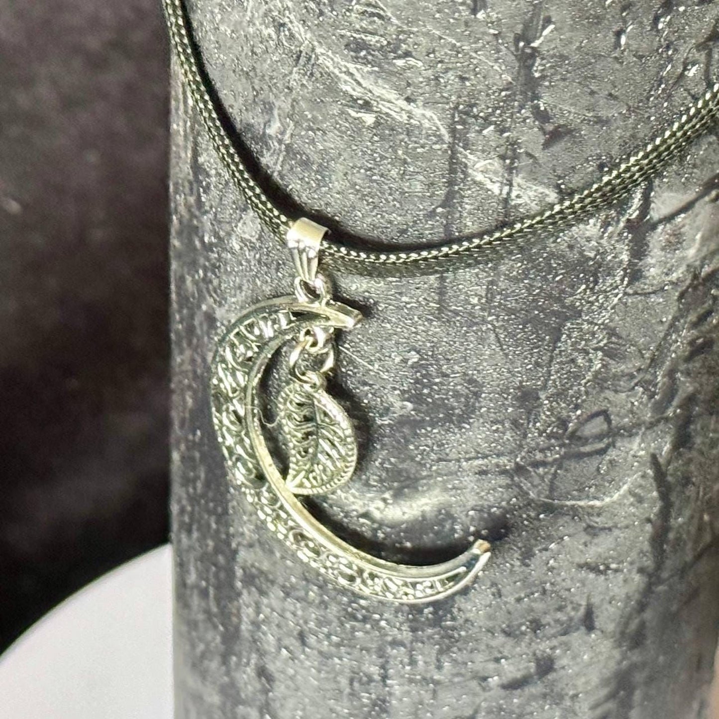 A silver necklace with a pendant featuring a crescent moon and leaf design.