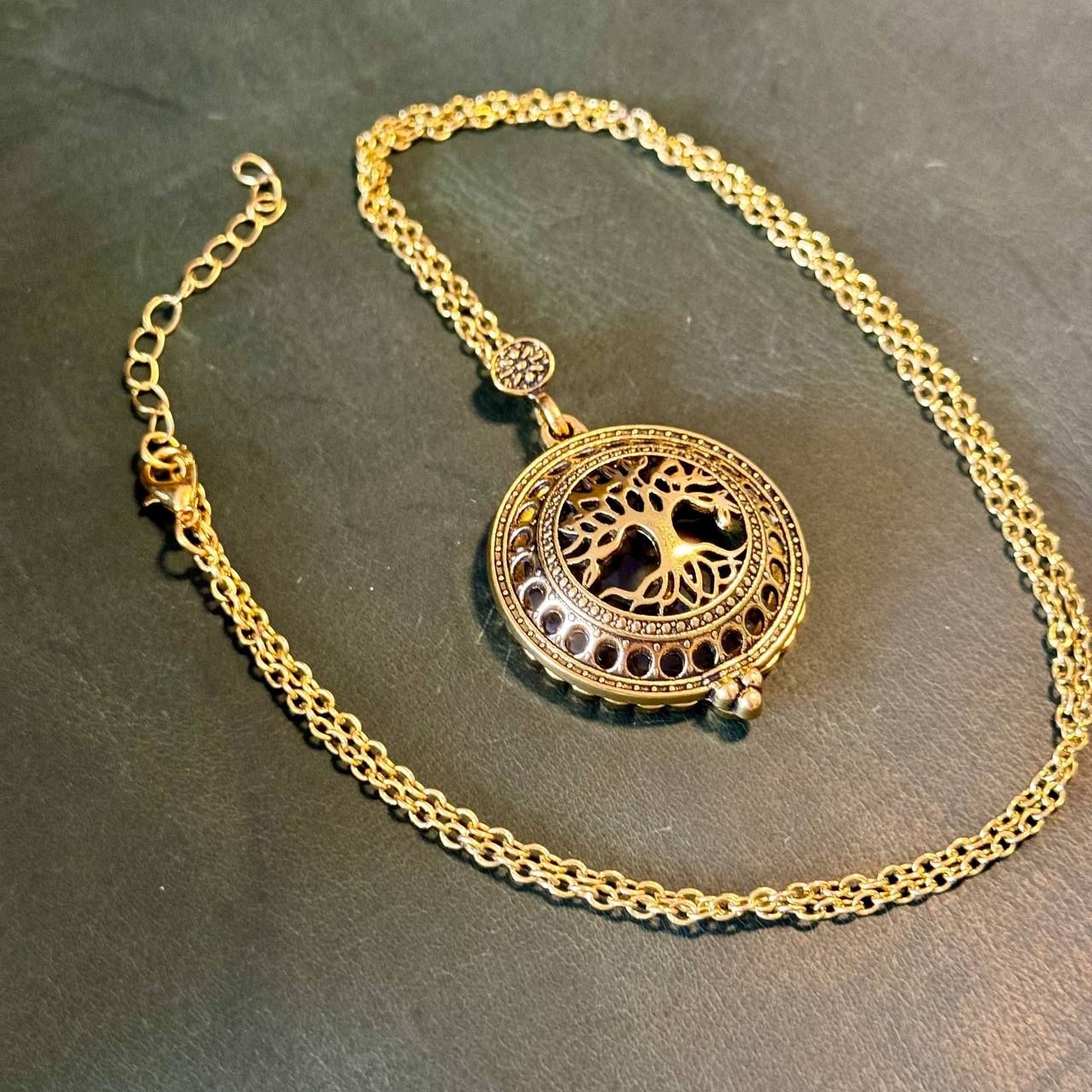 A gold-colored necklace with a circular pendant featuring a tree design.