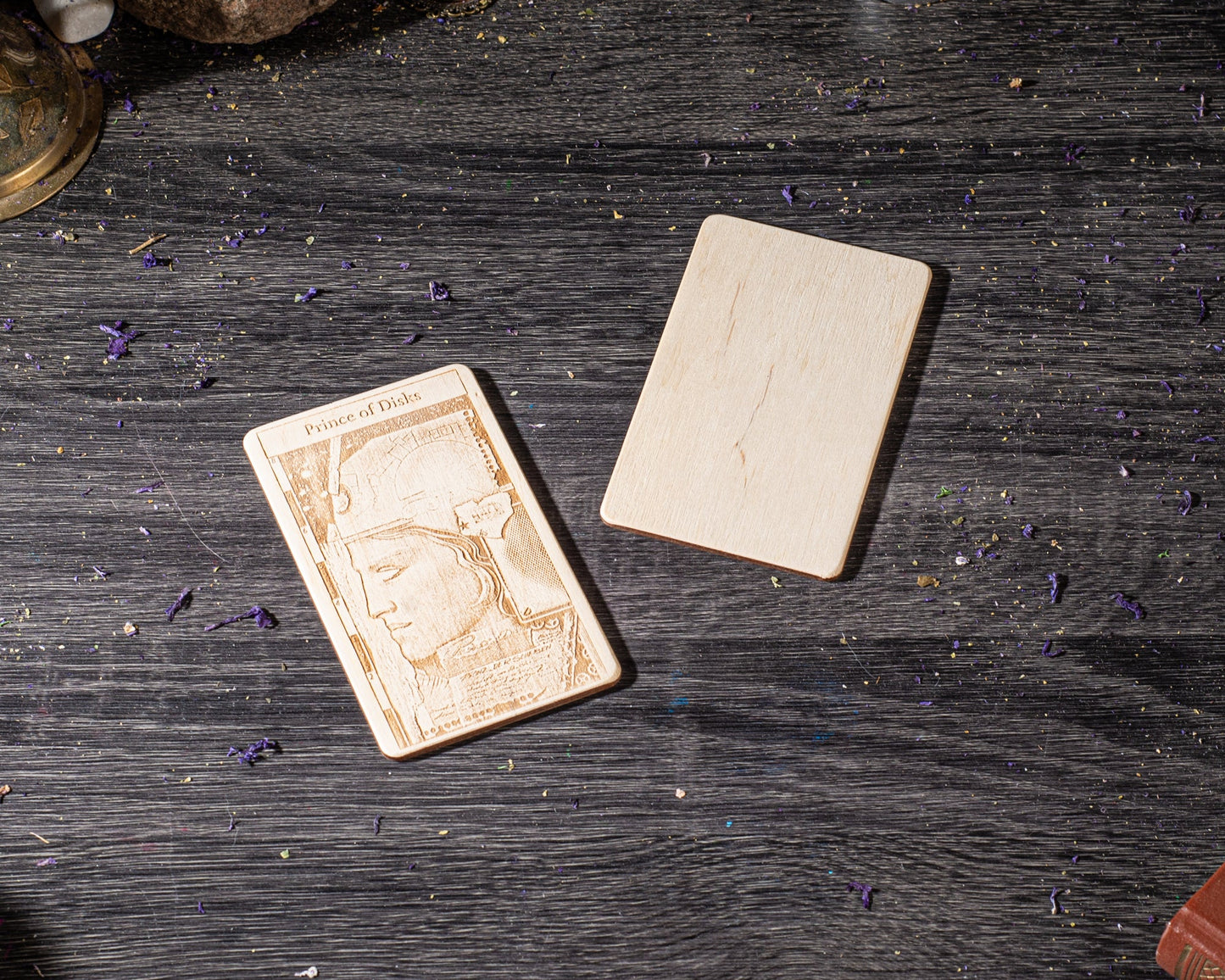 a wooden card with an embossed design, placed on a wooden surface with scattered purple flowers.
