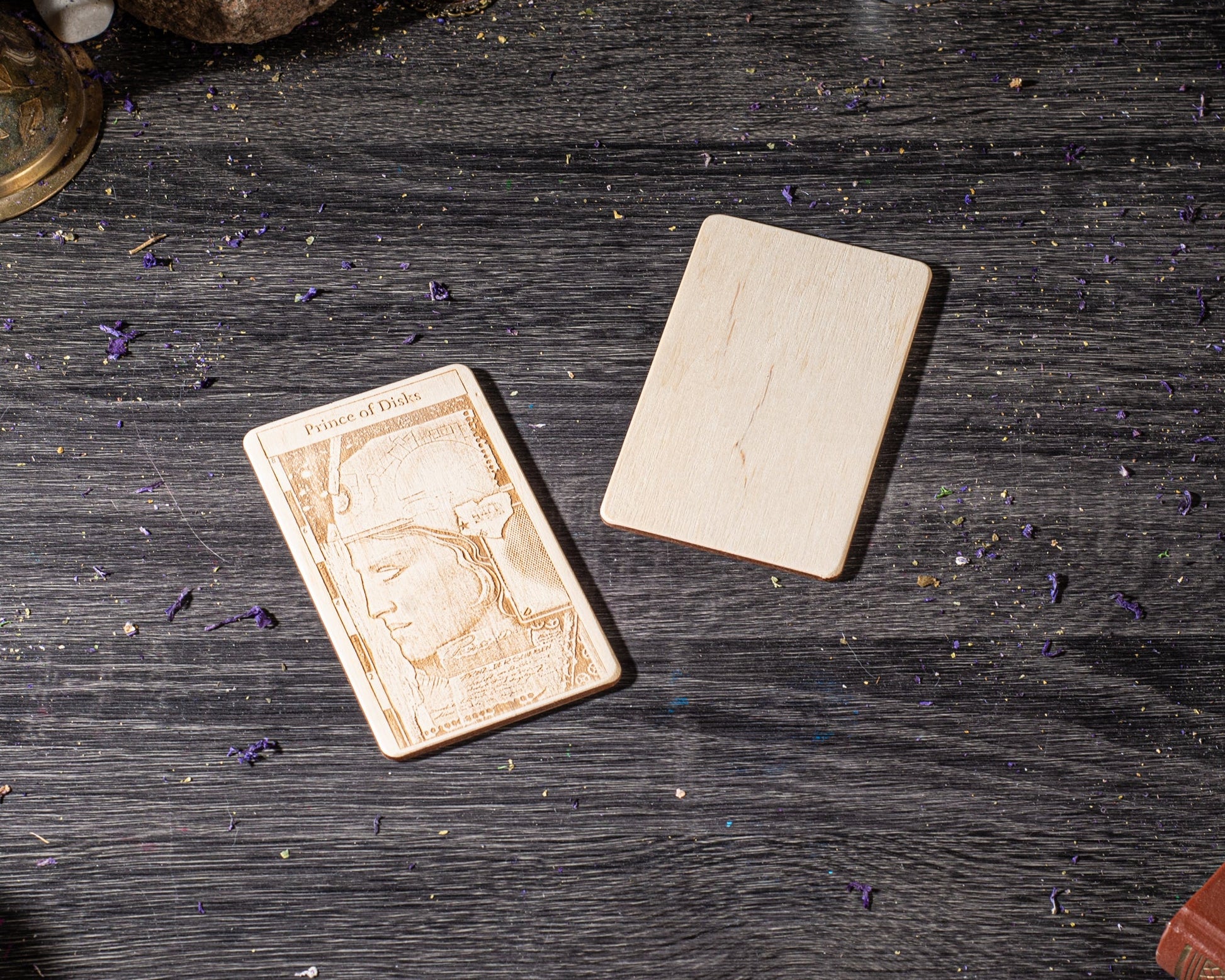 a wooden card with an embossed design, placed on a wooden surface with scattered purple flowers.