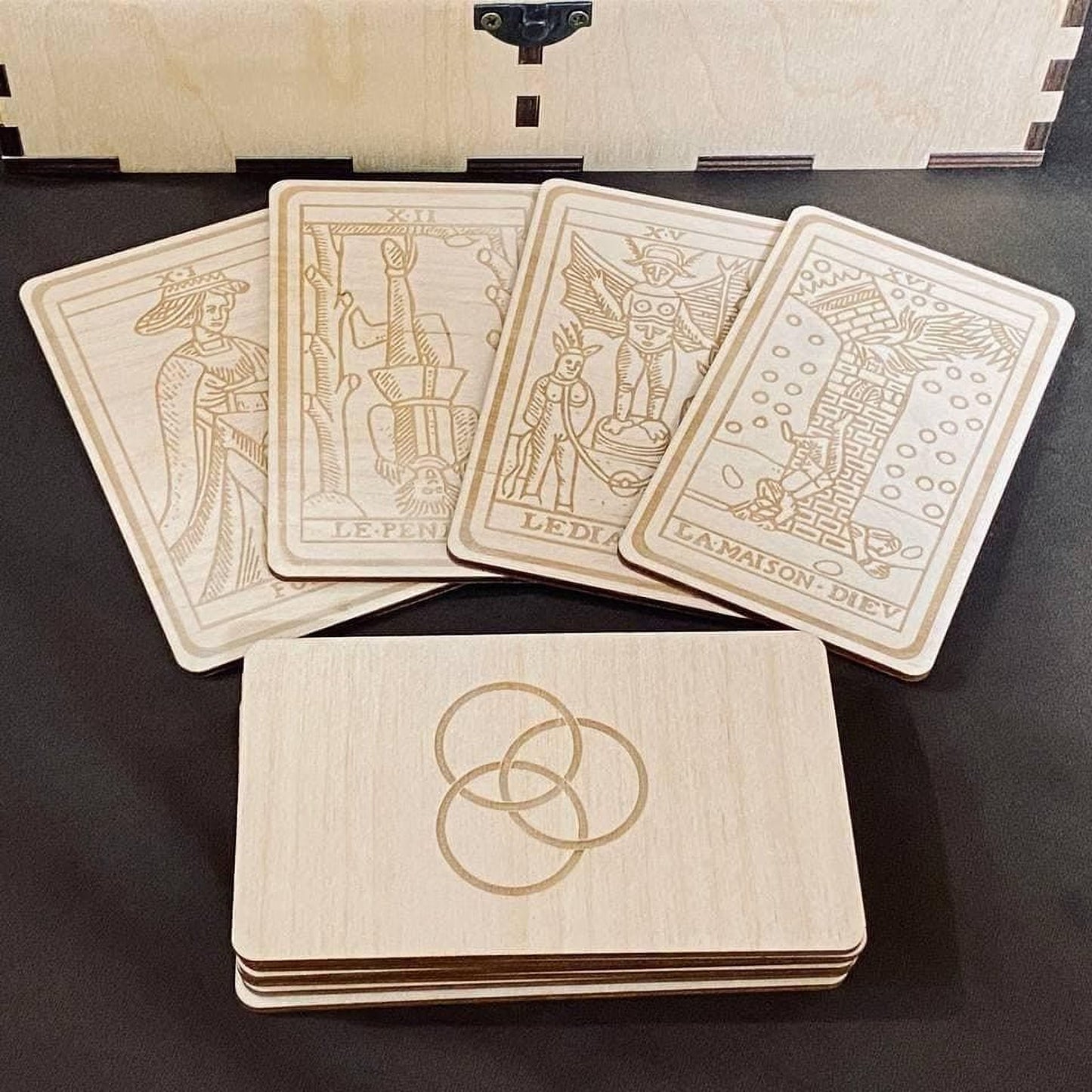 A set of wooden tarot cards and a wooden box with the same design, all featuring intricate engraved illustrations.