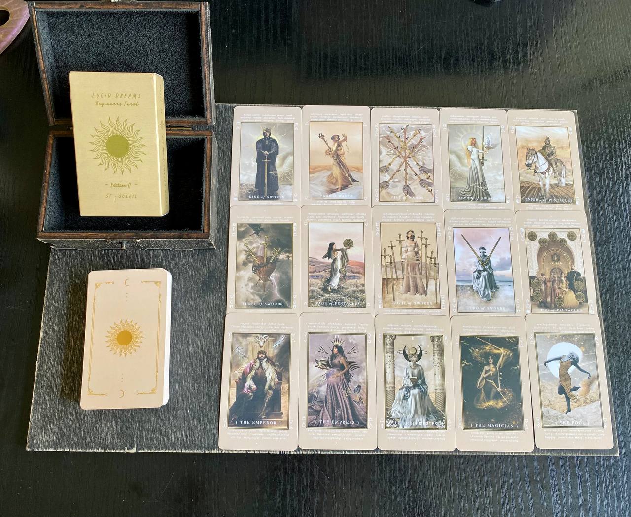 a tarot deck with various cards arranged on a wooden surface, along with a book and a box.