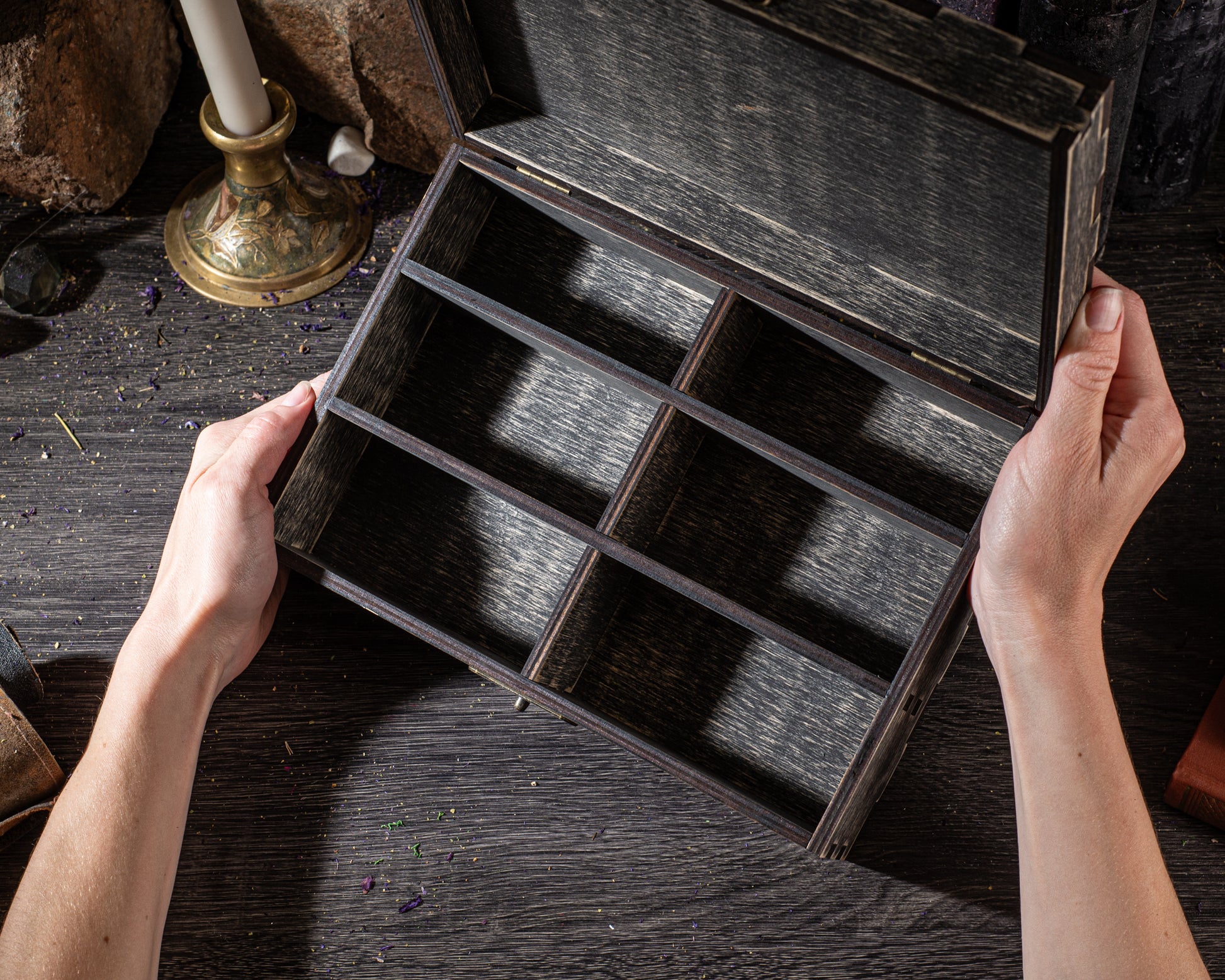 A person's hands are holding an open wooden box with six compartments on a dark wooden surface.