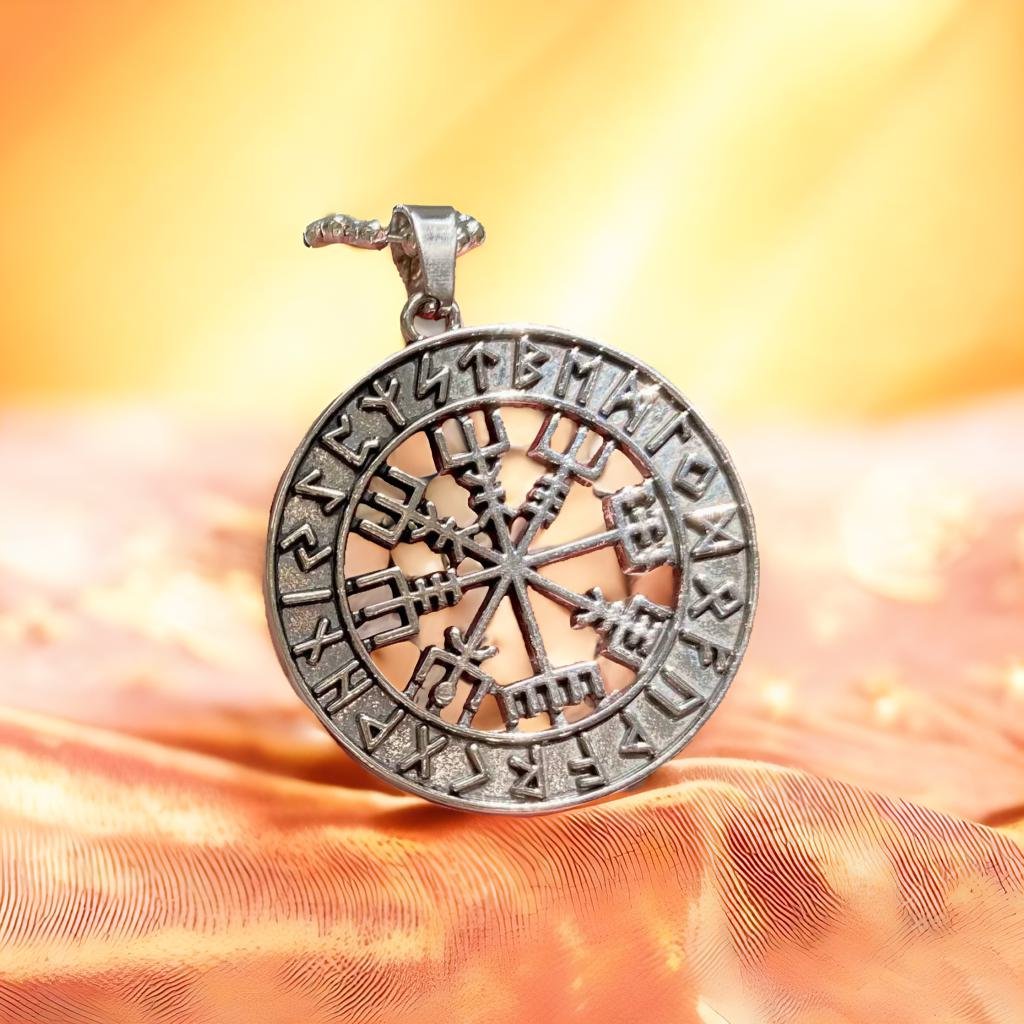 A silver pendant with a compass design, featuring various symbols and text, is displayed against a blurred orange background.
