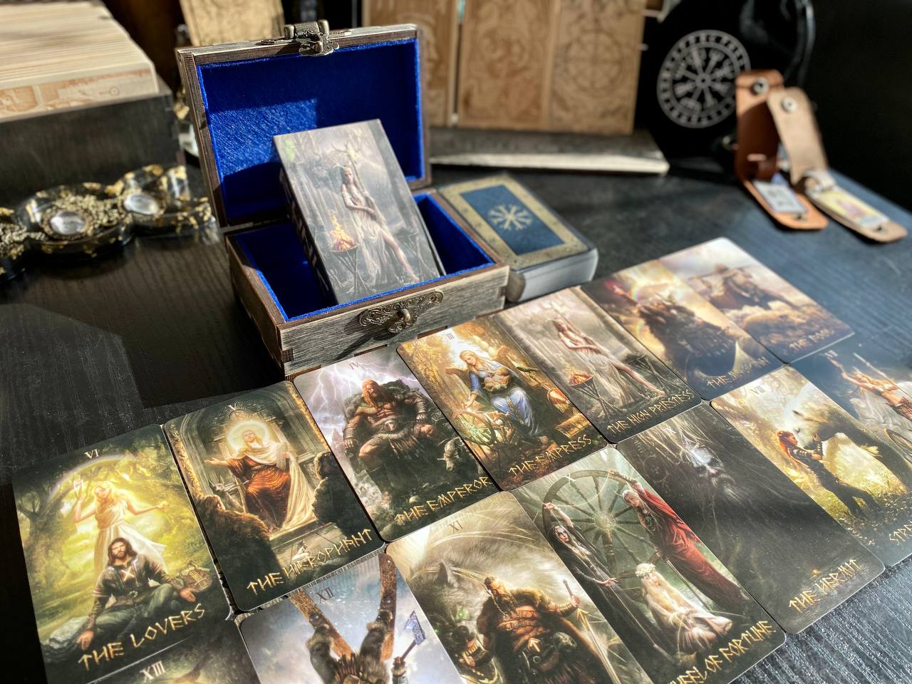 a collection of tarot cards spread out on a table, with a wooden box containing additional cards and a decorative item in the background.