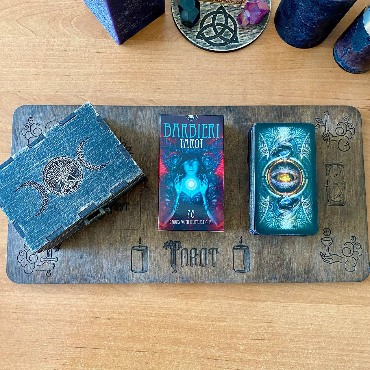 a collection of tarot cards and a wooden tray with the word "TAROT" printed on it, arranged on a wooden surface.