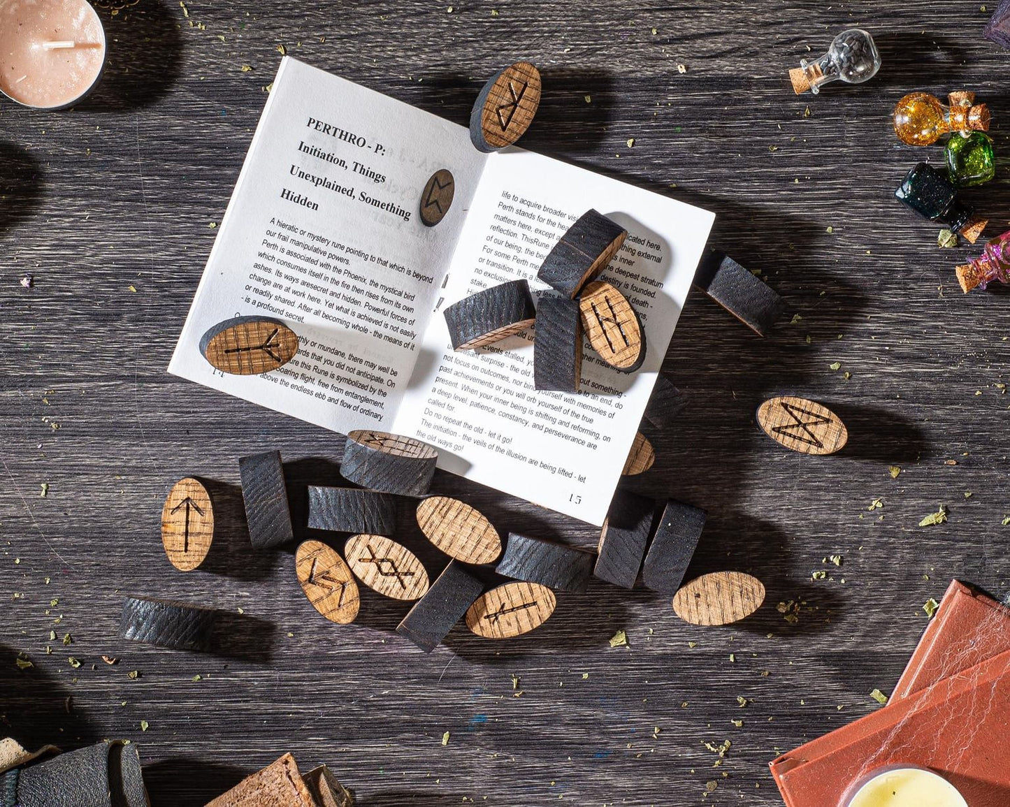 a book with a page displaying the text "PERTHO P. Unintended Things. Hidden" and several wooden objects with symbols on them, such as crosses and arrows, scattered on a wooden surface.