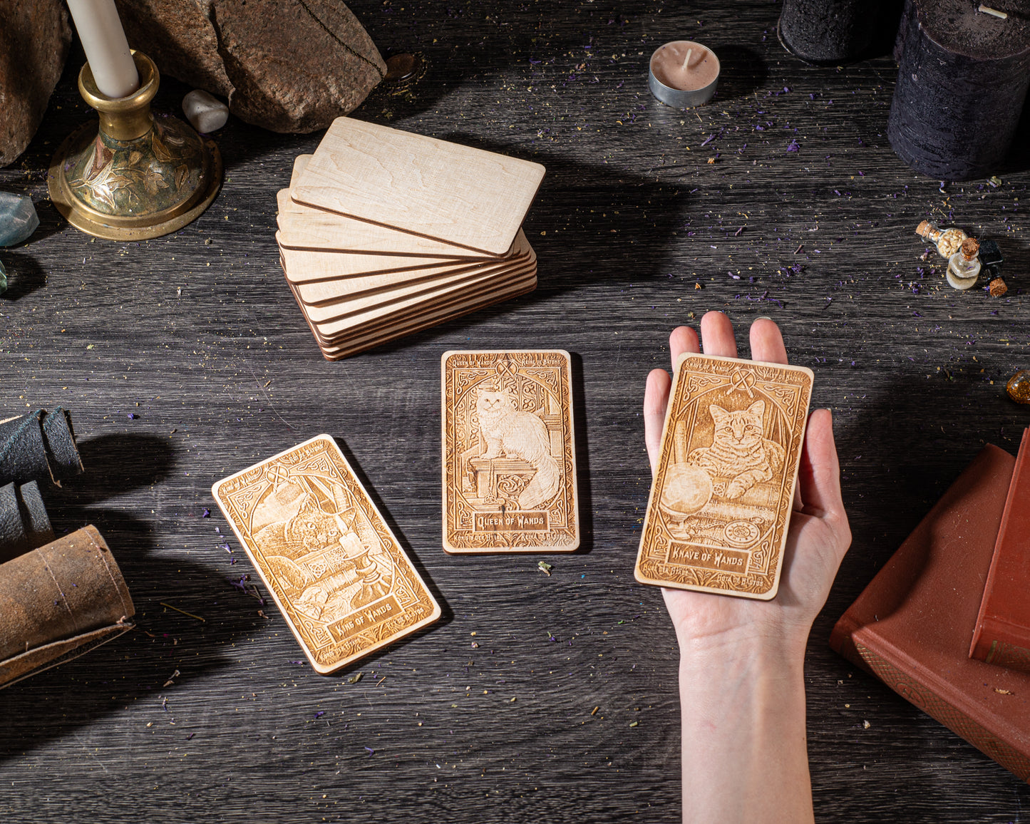 A hand is holding a wooden card with an illustration of a cat, surrounded by other wooden cards and objects on a dark wooden surface.