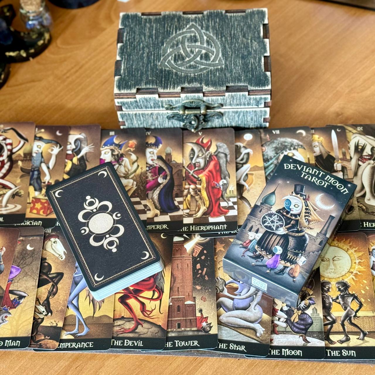 a collection of tarot cards and a wooden box with a Celtic knot design, arranged on a wooden surface.