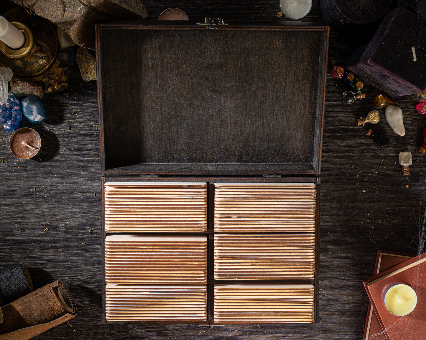 a wooden box with six compartments, placed on a dark wooden surface. The box appears to be empty, with no visible contents. There are also various objects scattered around the box, including candles, books, and other items, creating a cluttered and disorganized appearance.