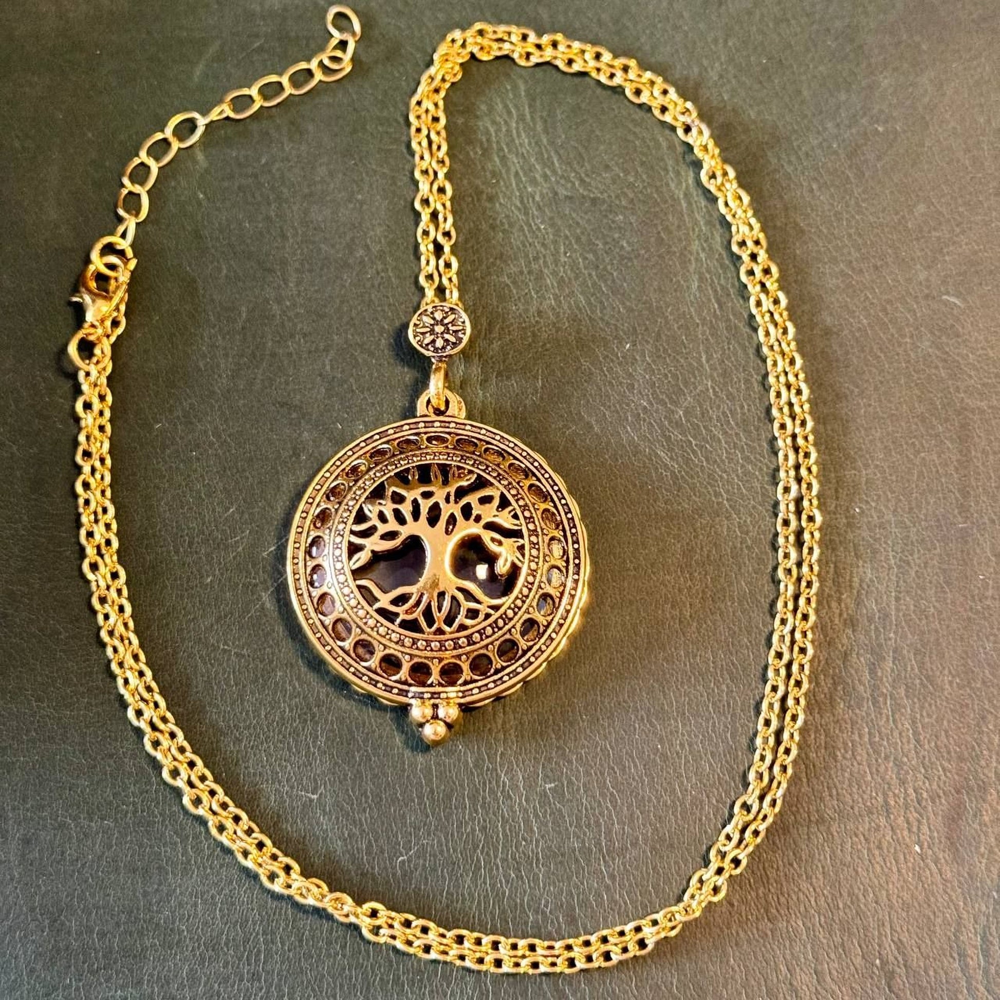 A gold-colored necklace with a circular pendant featuring a tree design.