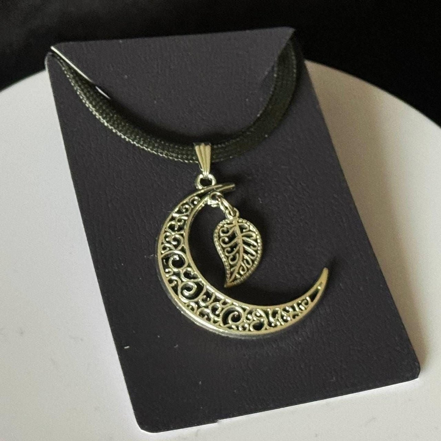 A silver-colored pendant necklace with a crescent moon design and a leaf-shaped charm hanging from it.