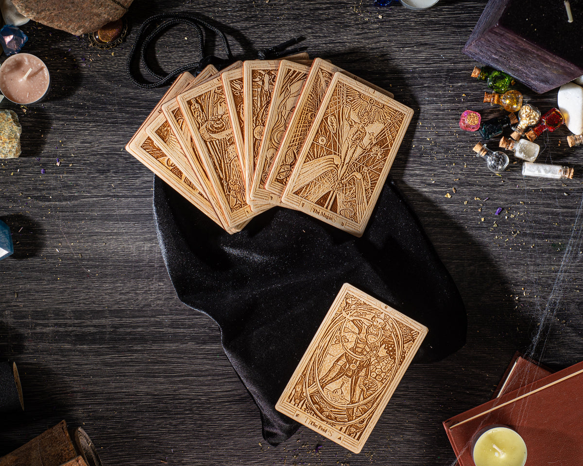 a collection of tarot cards and other items arranged on a wooden surface, including a black velvet pouch, a candle, and various small objects.