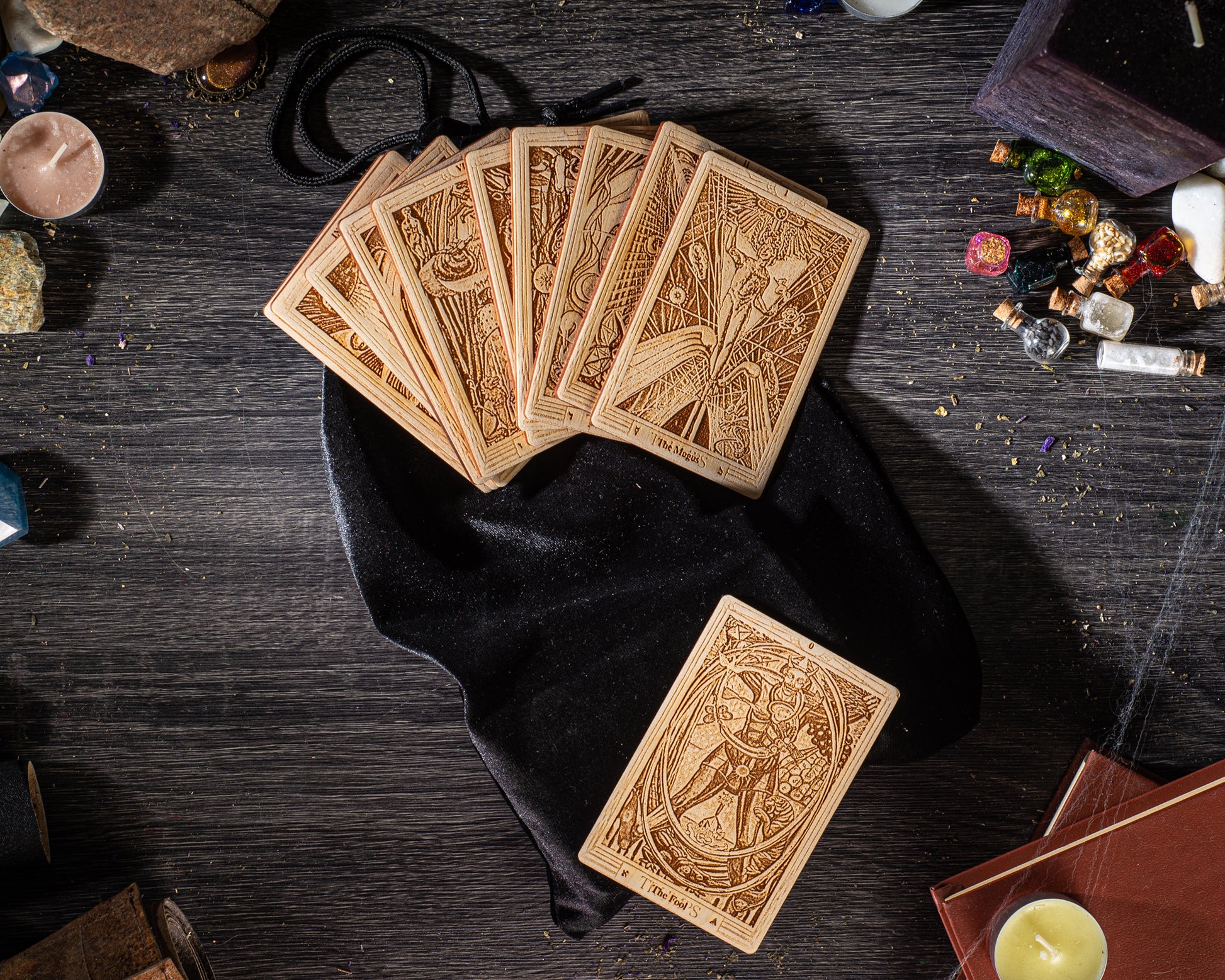 a collection of tarot cards and other items arranged on a wooden surface, including a black velvet pouch, a candle, and various small objects.