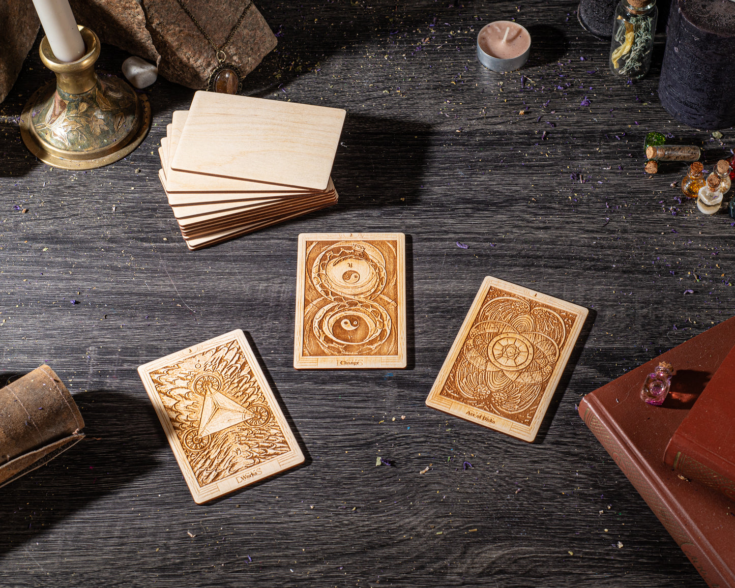 three wooden tarot cards with intricate designs, placed on a dark wooden surface alongside various objects such as candles, crystals, and books.