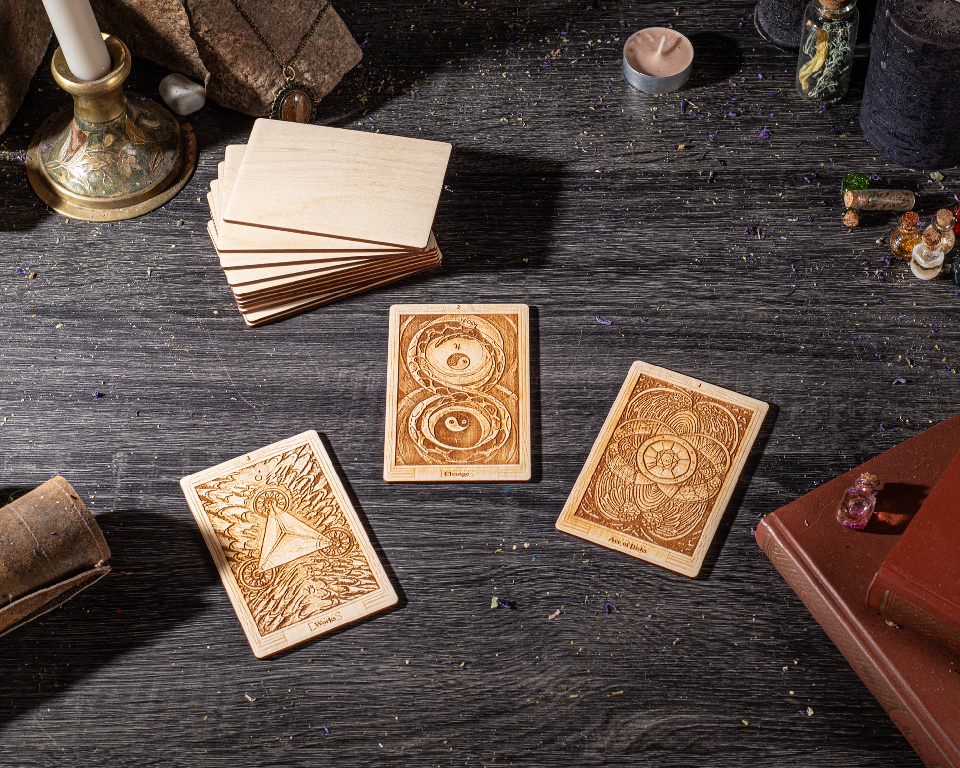 three wooden tarot cards with intricate designs, placed on a dark wooden surface alongside various objects such as candles, crystals, and books.