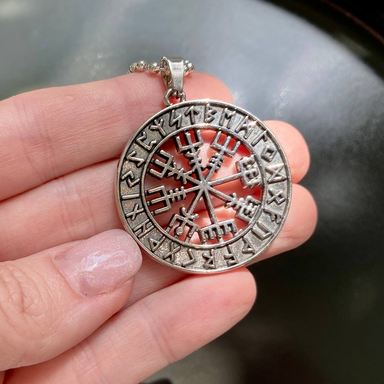 A silver pendant necklace with a circular design featuring a compass rose and various symbols.