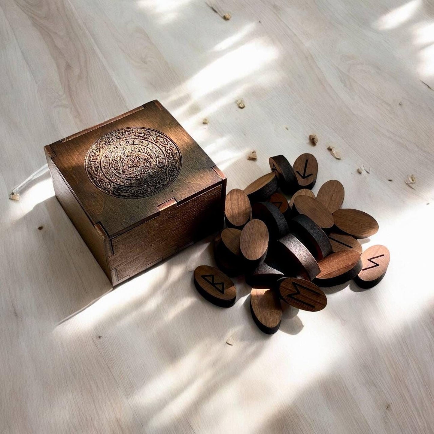 A wooden box with a carved design on the lid and a pile of wooden blocks with symbols on them are placed on a wooden surface.