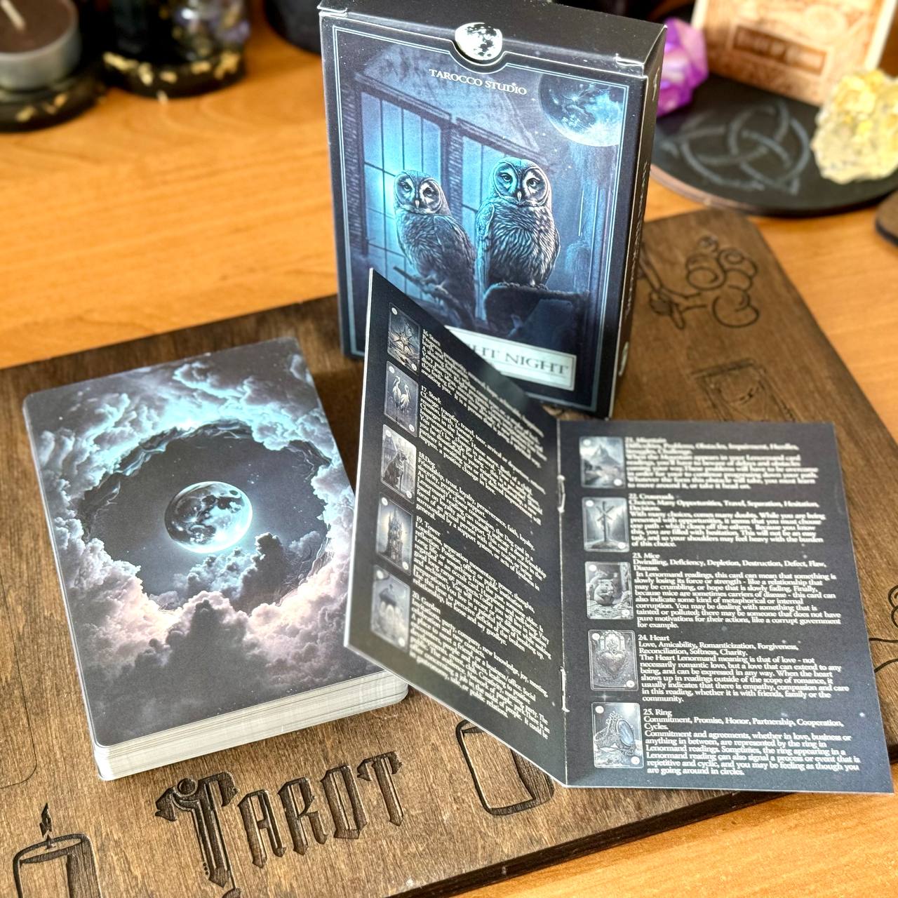 a tarot deck with a wooden board displaying the word "Tarot" and a box of the deck with a picture of two owls on the cover.