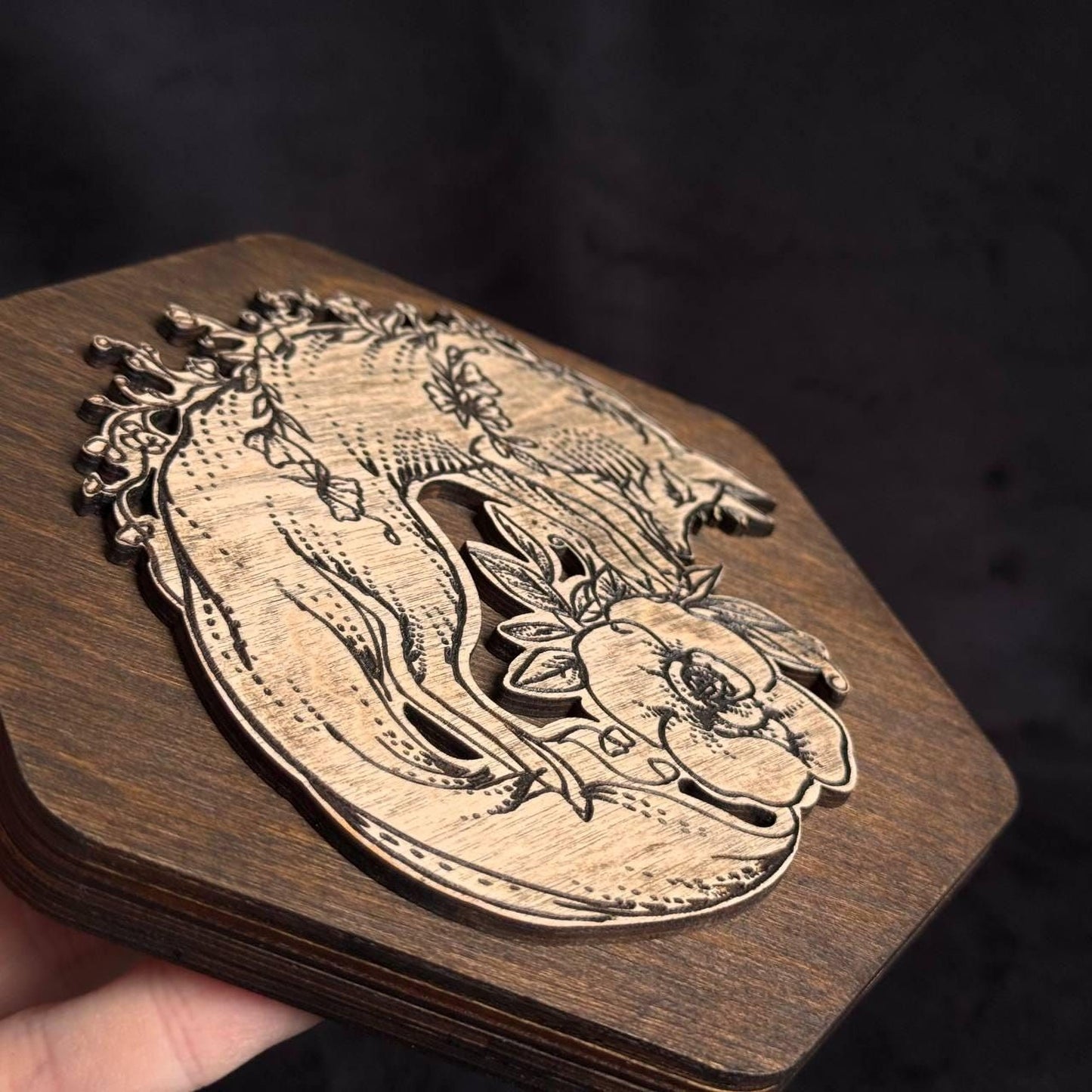 A wooden object with a carved design featuring a floral motif and a stylized animal figure.