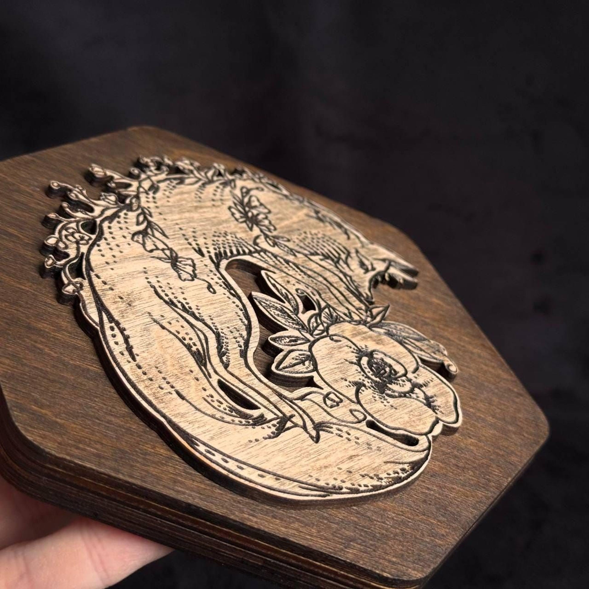 A wooden object with a carved design featuring a floral motif and a stylized animal figure.