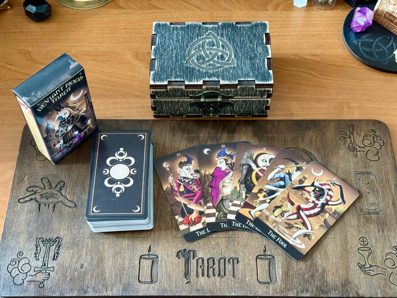 a tarot deck, a wooden table, and a wooden box with a Celtic knot design. The tarot cards are spread out on the table, and the wooden box is placed next to them.