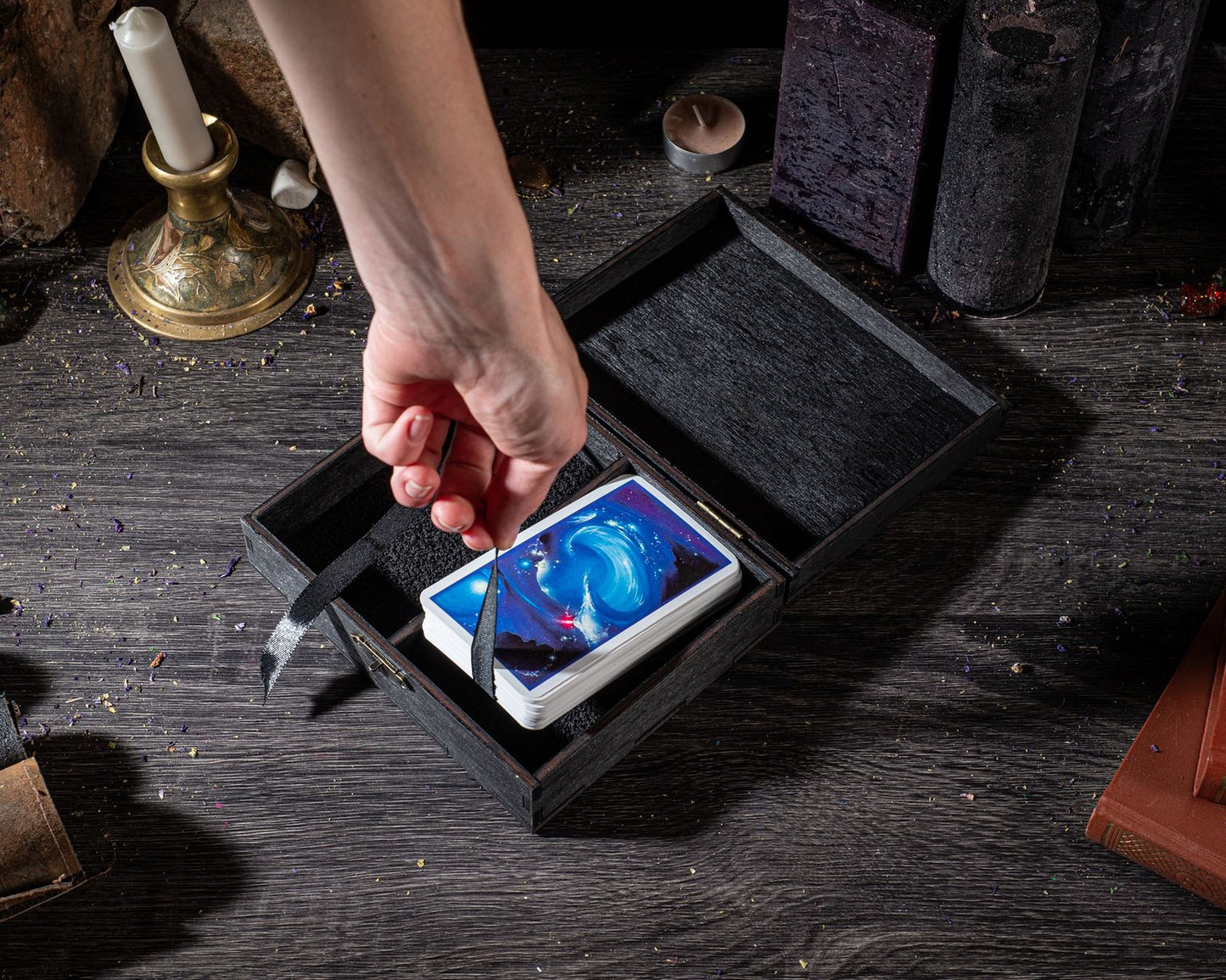 A hand is holding a card from a deck, with the card partially visible inside a wooden box on a wooden surface.