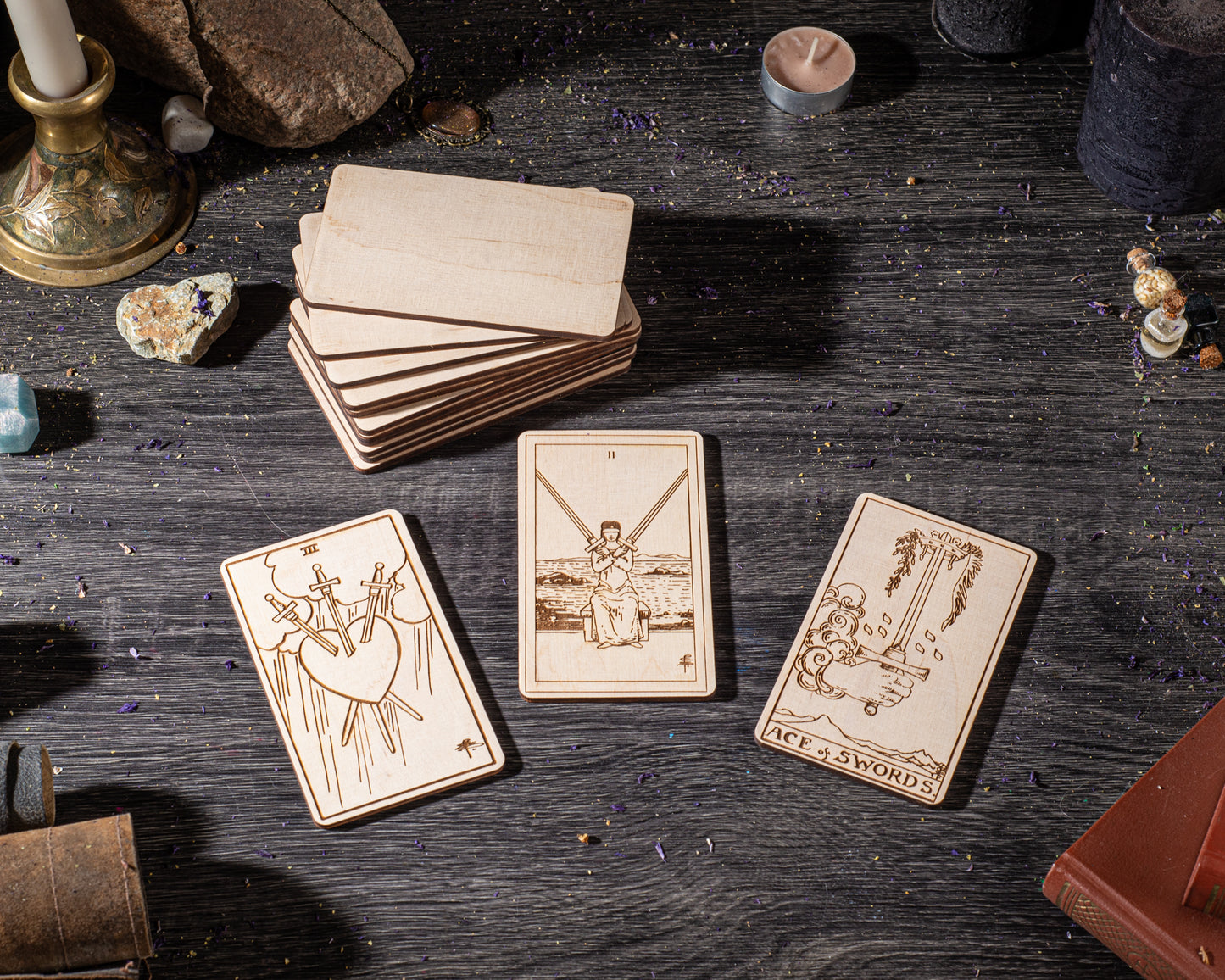 three wooden tarot cards with illustrations and text, arranged on a wooden surface with various objects such as a candle, rocks, and a book.
