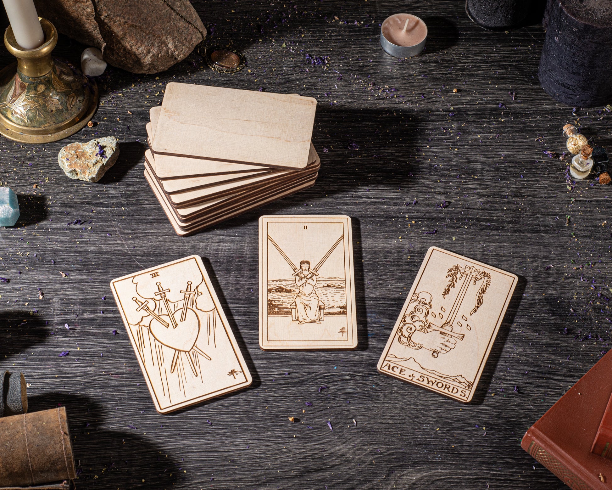 three wooden tarot cards with illustrations and text, arranged on a wooden surface with various objects such as a candle, rocks, and a book.