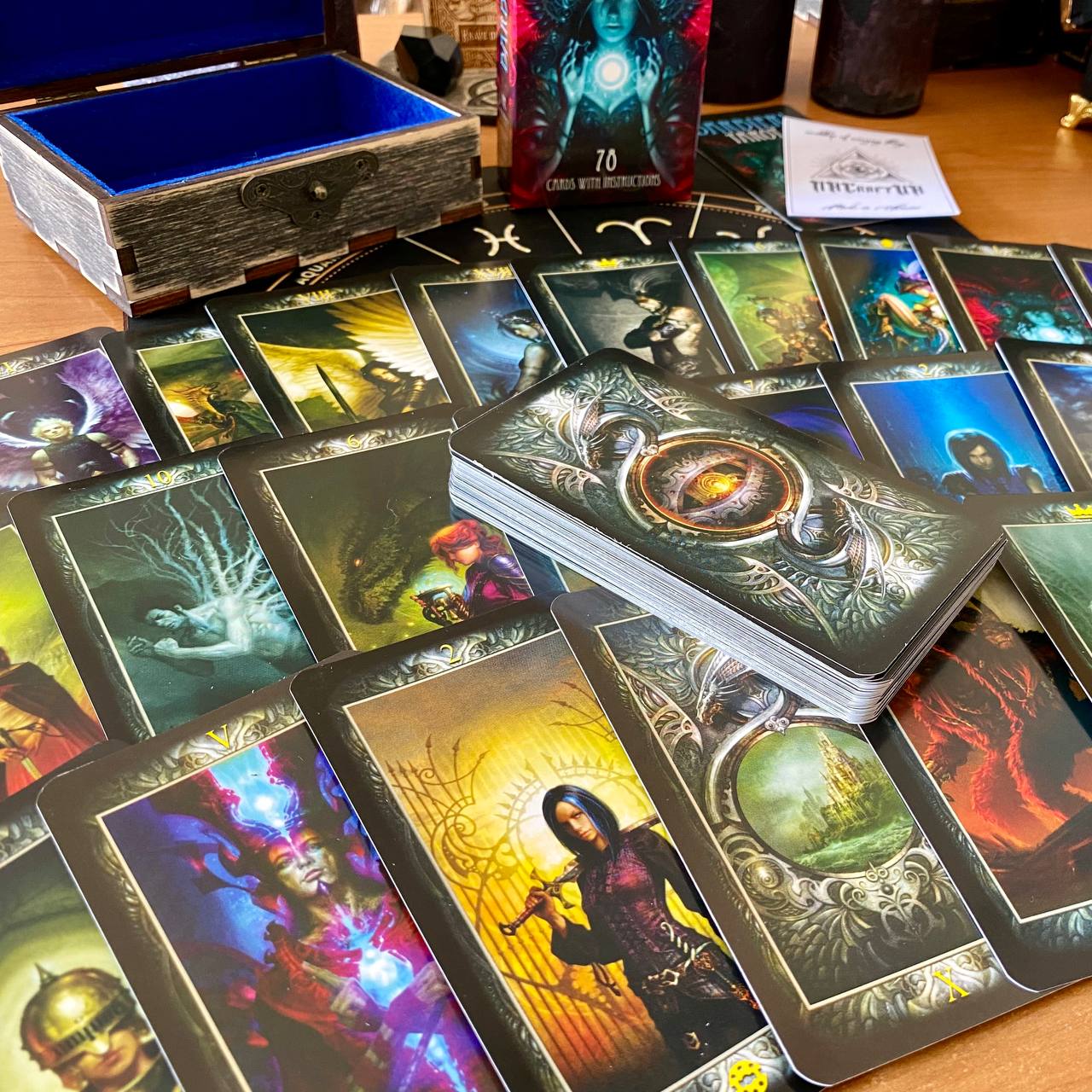 a collection of tarot cards and a wooden box, with various artistic and fantastical designs on the cards and the box.
