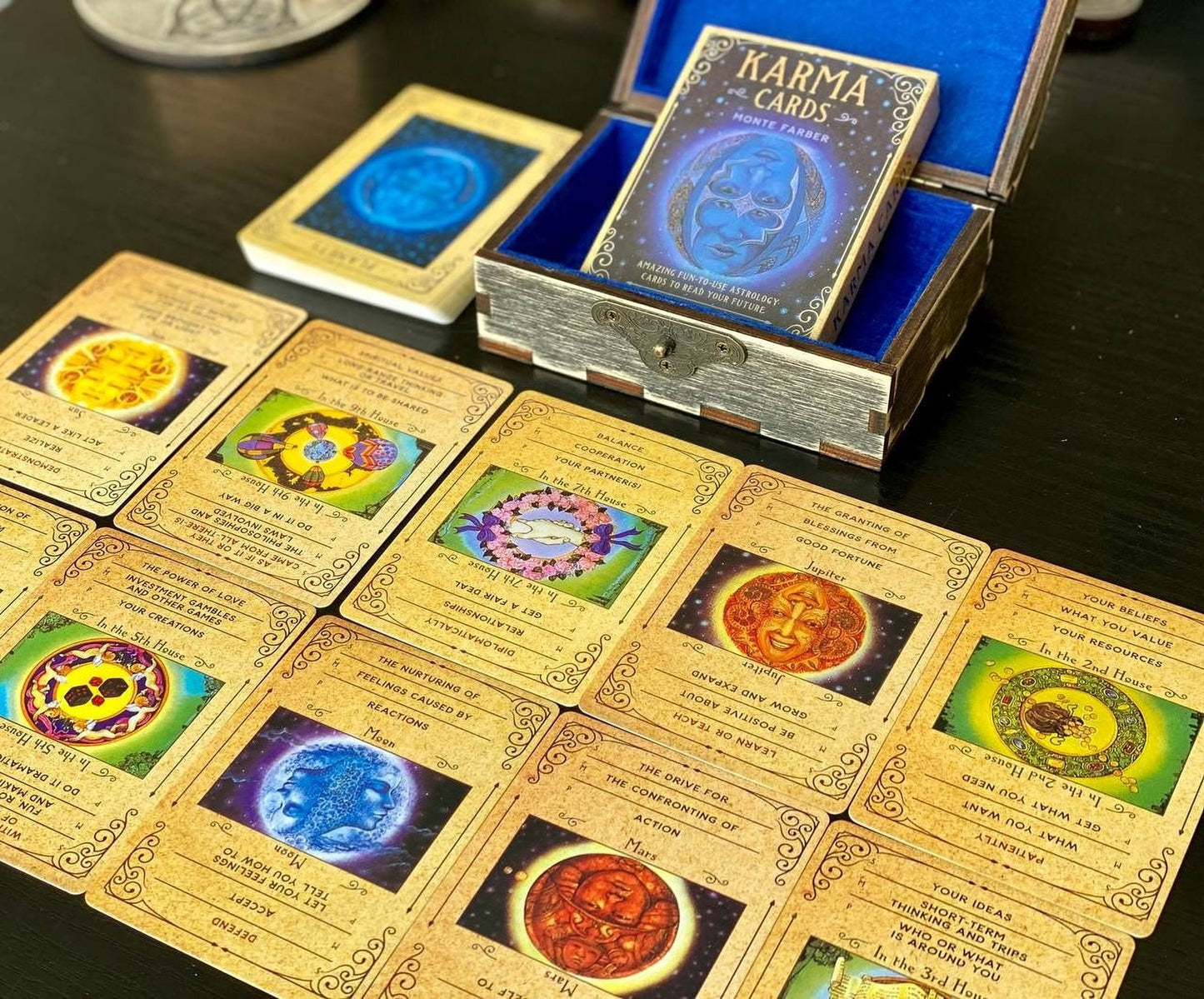 a collection of cards and a box with the title "KARMA CARDS" on a dark wooden surface. The cards are arranged in rows, each featuring a different design and symbol. The box is open, revealing the cards inside.
