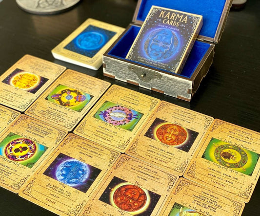 a collection of cards and a box with the title "KARMA CARDS" on a dark wooden surface. The cards are arranged in rows, each featuring a different design and symbol. The box is open, revealing the cards inside.