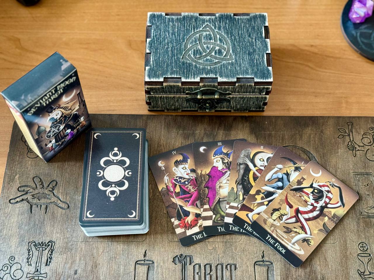 a tarot deck, a wooden box, and a deck of playing cards arranged on a wooden surface.