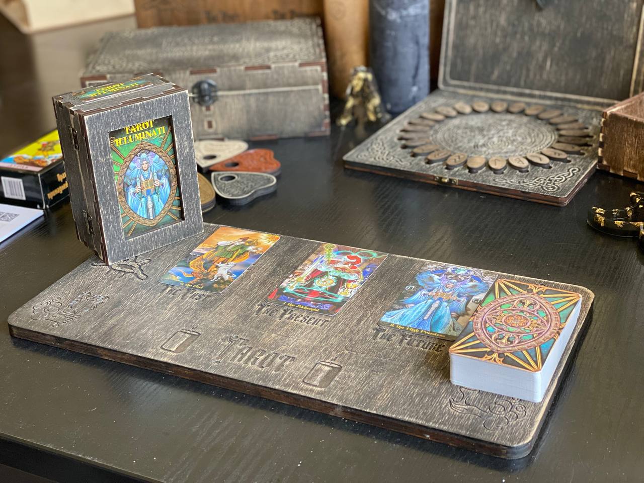 a tarot card reader's table with a wooden tray displaying three tarot cards, a small wooden box, and various other items on a wooden surface.